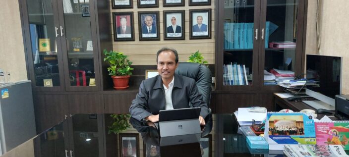 Foto Wakil Rektor I Bidang Akademik saat duduk menghadap laptop di ruangannya